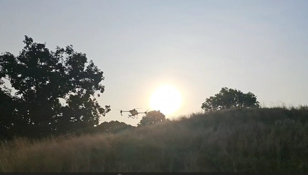 Agras spray drone flying over a native hillside at sunset